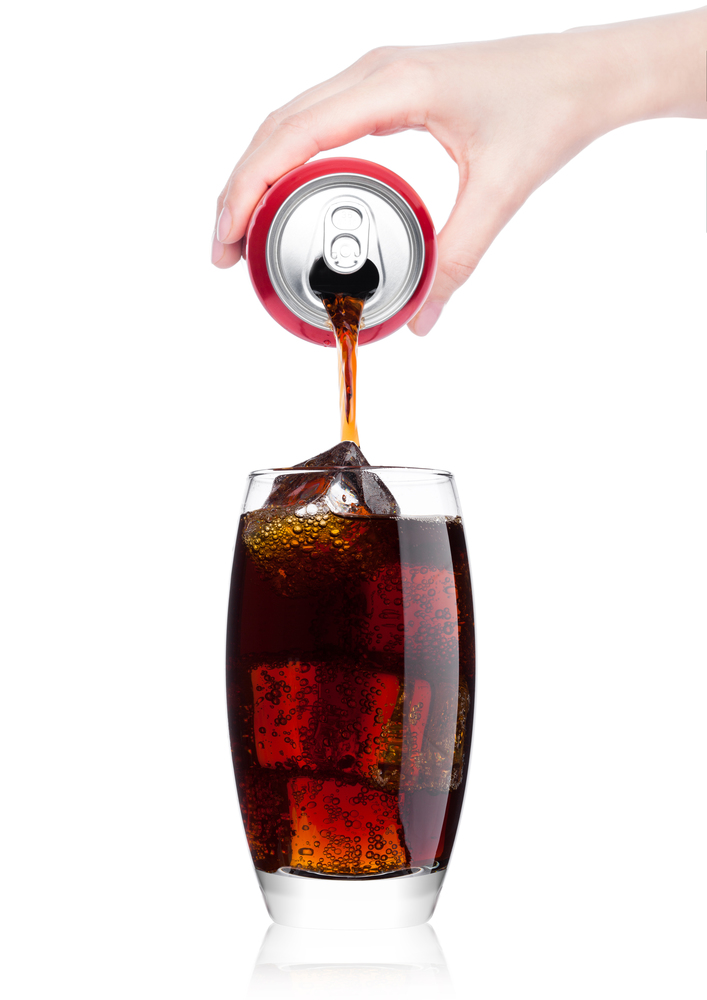 Female hand pouring cola soda drink from aluminium can to glass  with ice cubes on white background