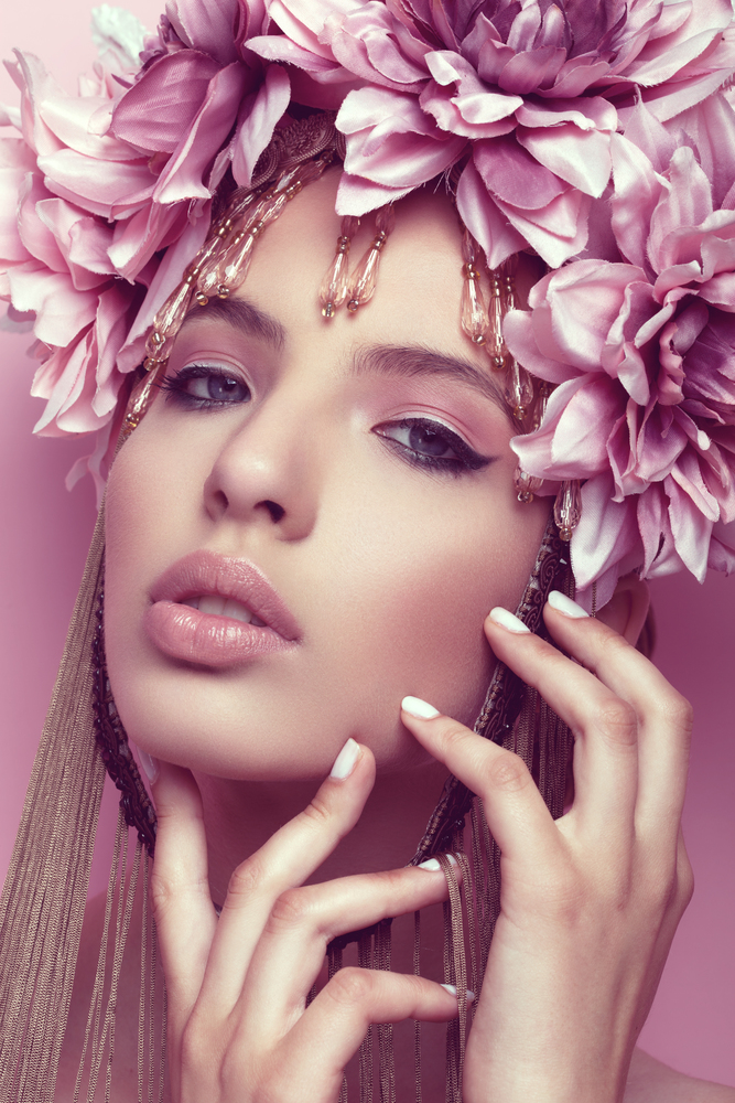 Beautiful woman with flower crown and makeup on pink background holding hand under her chin