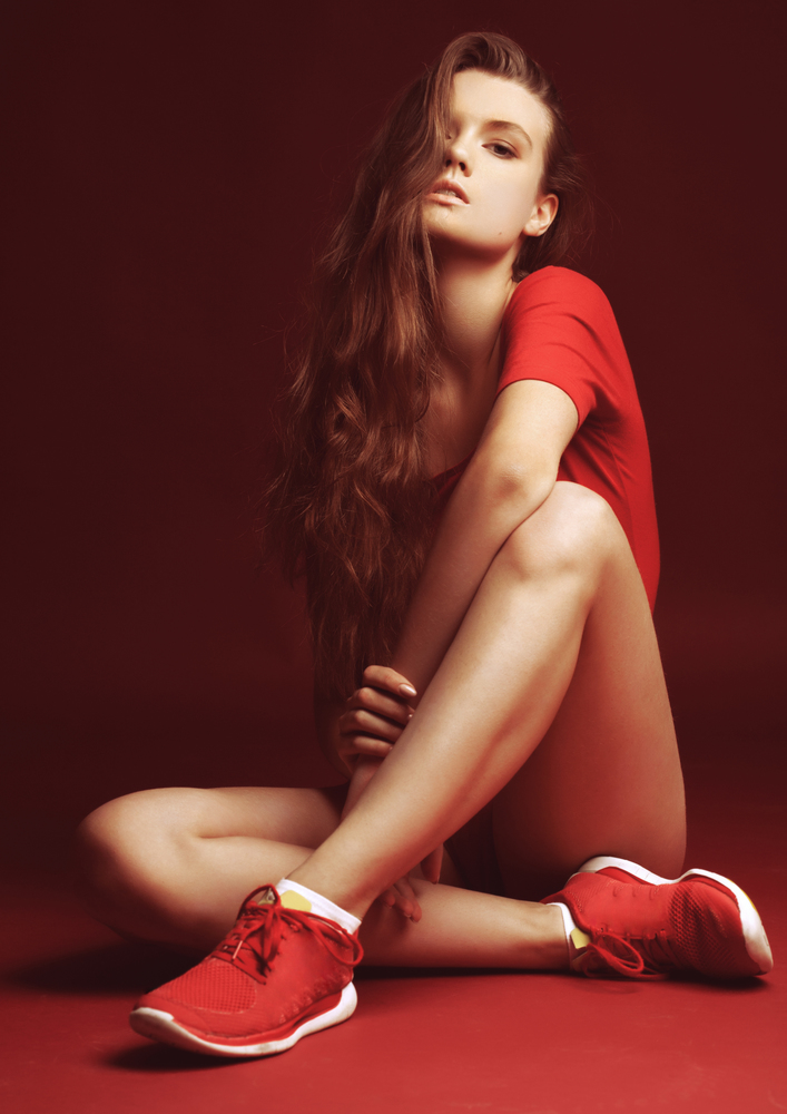 Beautiful girl in red sport body on red background with long hair