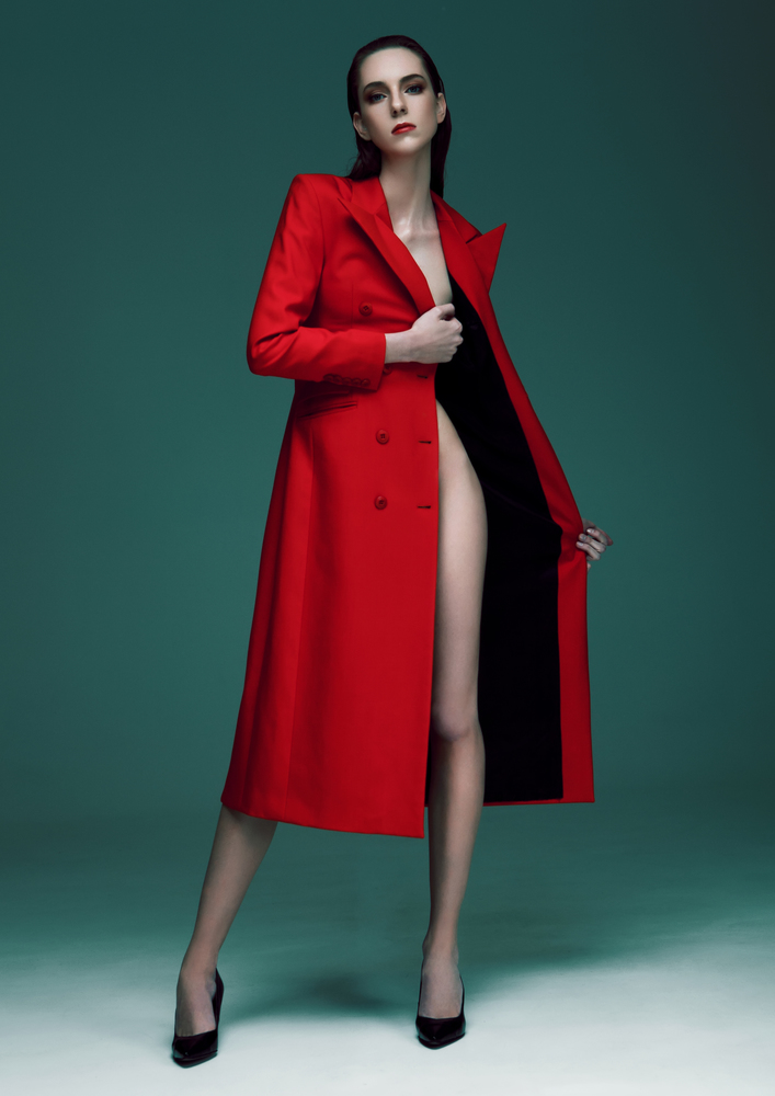 Fashion model with wet hair wearing red long coat on green background