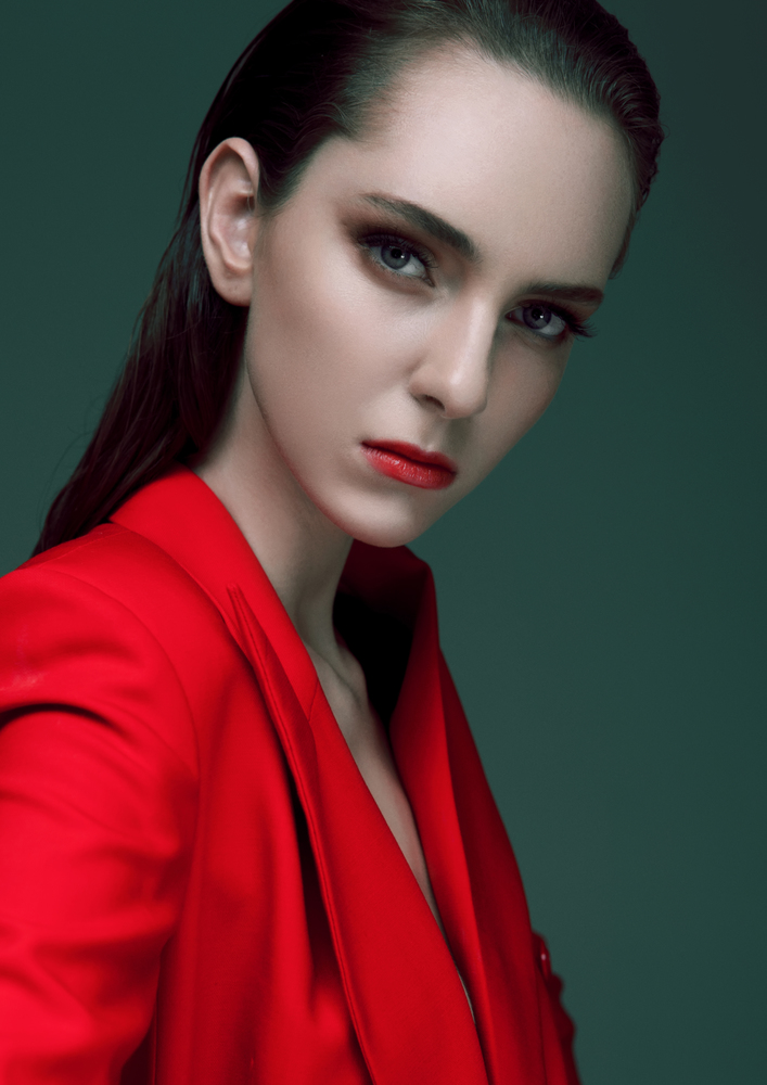 Fashion model with wet hair wearing red long coat on green background. Fashion portrait.