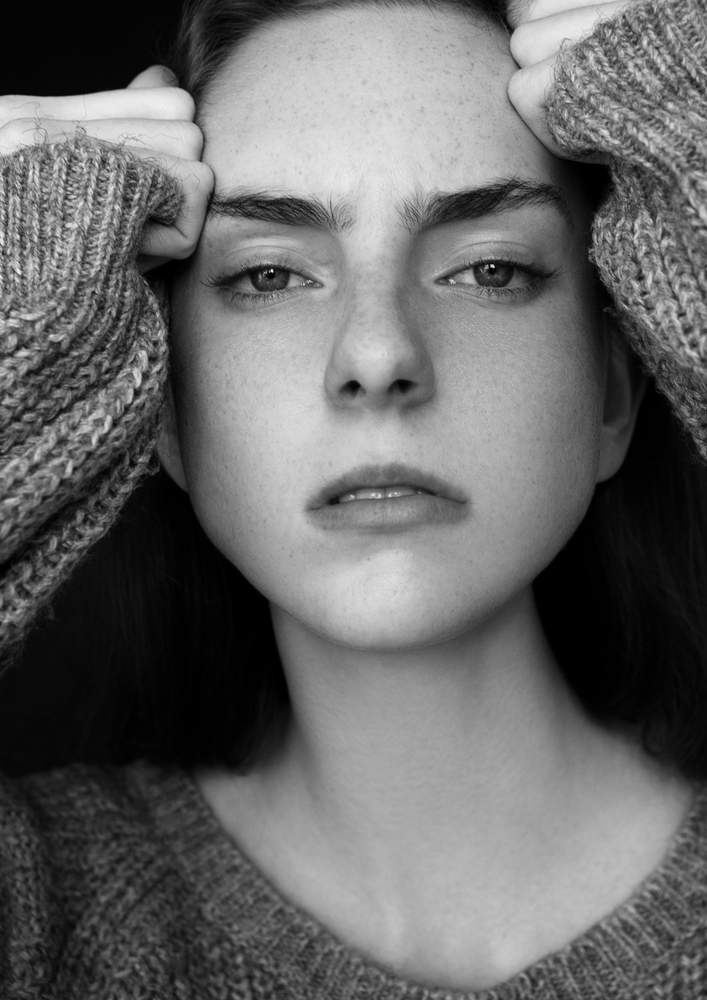 Model portrait test with young beautiful fashion model wearing grey jumper on black background.Dramatic portrait.