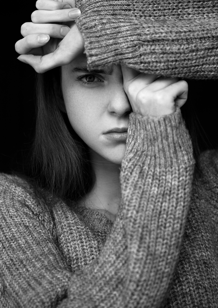 Model portrait test with young beautiful fashion model wearing grey jumper on black background.Dramatic portrait.