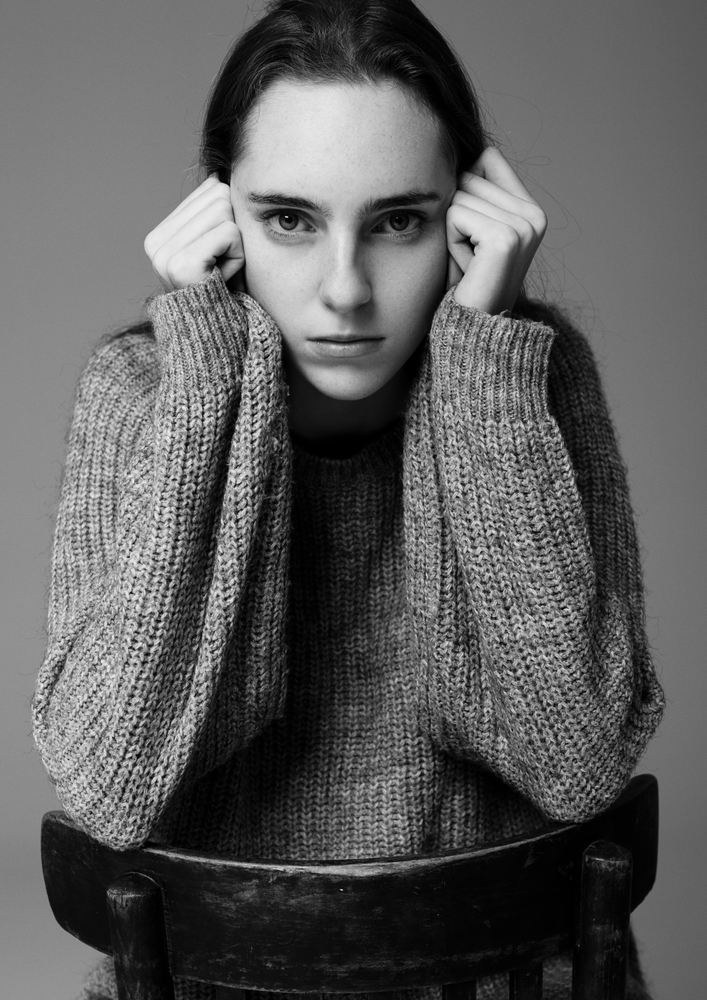 Model portrait test with young beautiful fashion model wearing grey jumper on grey background.Sitting on old grunge chair