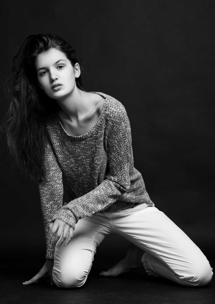Model test portrait with young beautiful fashion model posing on grey background. Grey jumper with white jeans