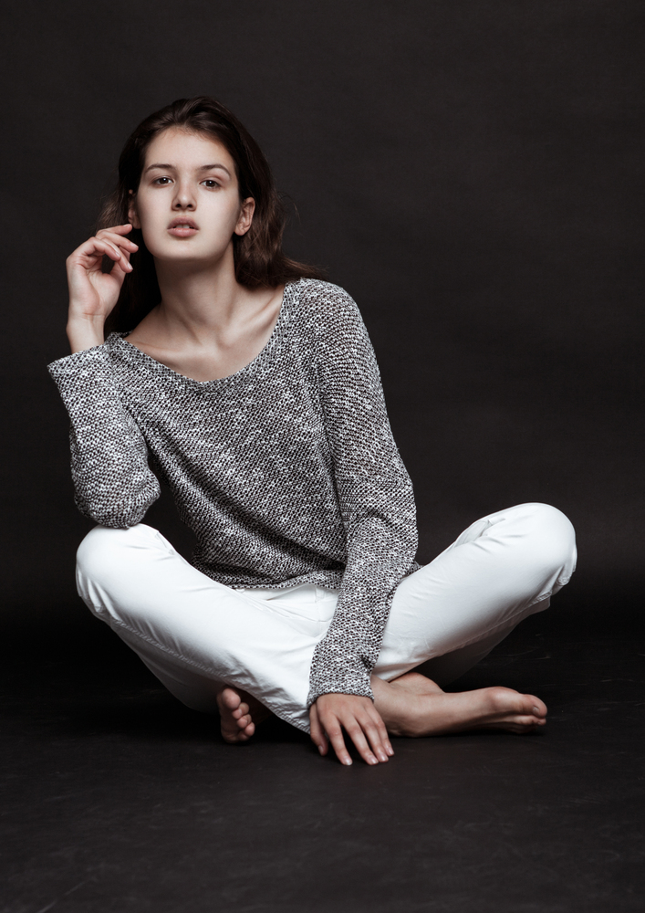 Model test portrait with young beautiful fashion model posing on grey background. Grey jumper with white jeans