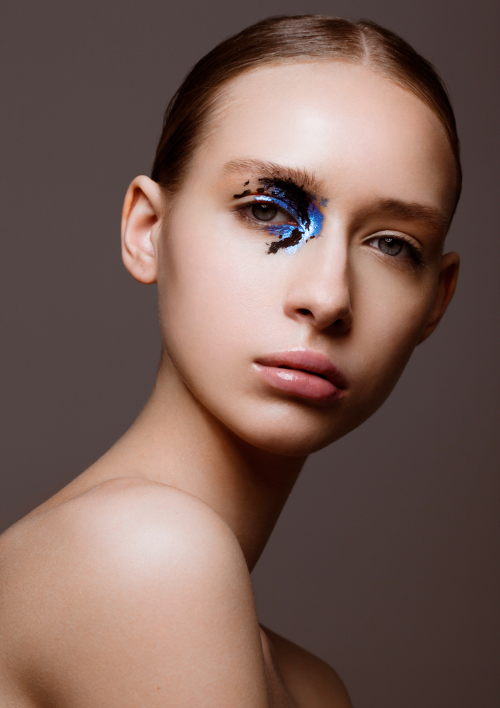 Beauty fashion model with creative black and blue makeup on dark grey background