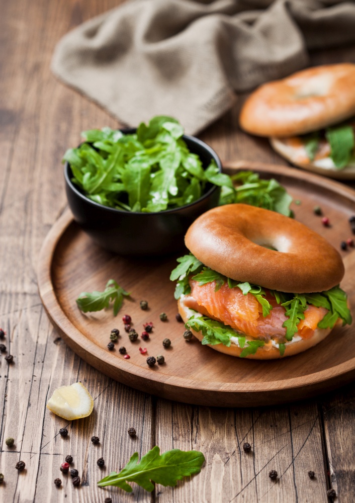 Fresh healthy organic sandwich with bagel and salmon, cream cheese and wild rocket in bowl plate on wooden table background with towel.