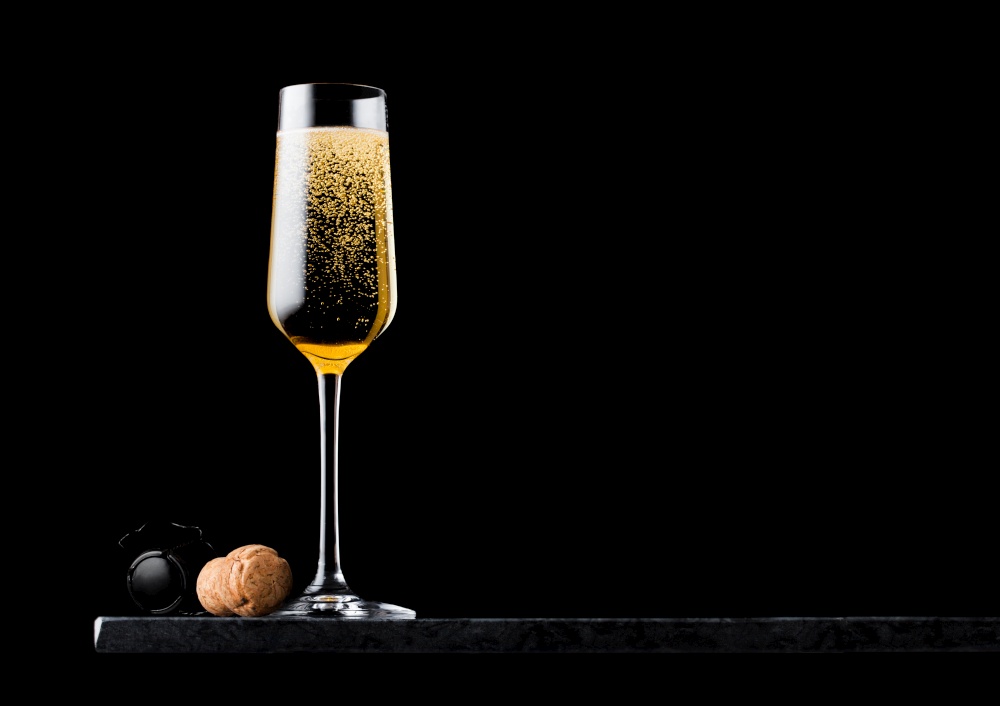 Elegant glass of yellow champagne with cork and wire cage on black marble board on black background.