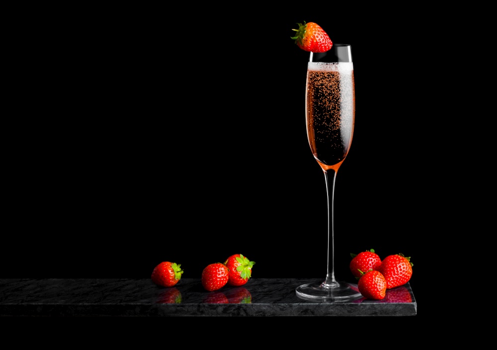Elegant glass of pink rose champagne with strawberry on top on black marble board on black background.