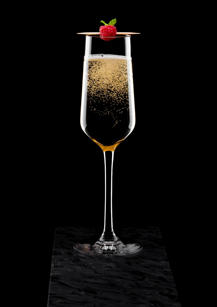Elegant glass of yellow champagne with rasspbery on stick on black marble board on black