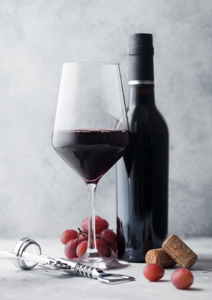 Mini bottle of red wine with glass and corks with steel corkscrew and grapes on light table background.