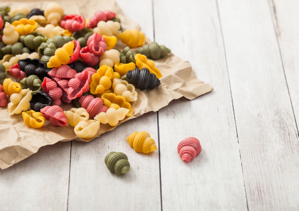 Homemade conchiglioni tricolore pasta in brown paper on white wooden background. Black, red and green pasta