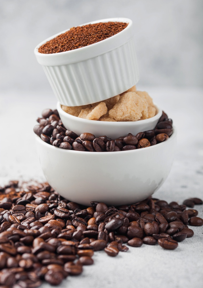 Three bowls on top of each other with fresh raw coffee beans and powder with cane sugar on light table background.