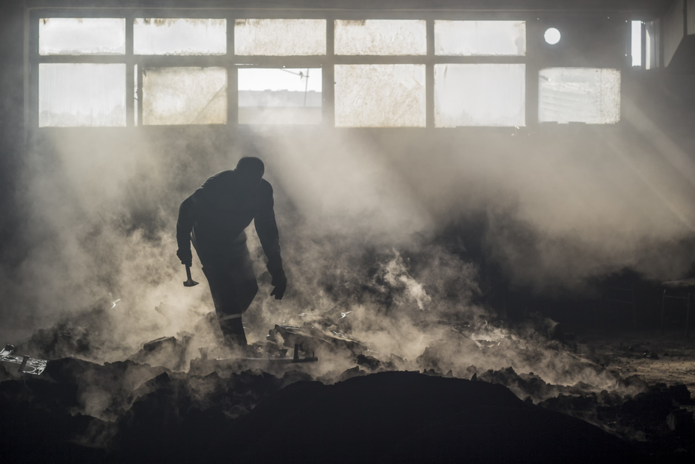 a foundry worker silhouette with his hammer,working environment with high temperature and fog