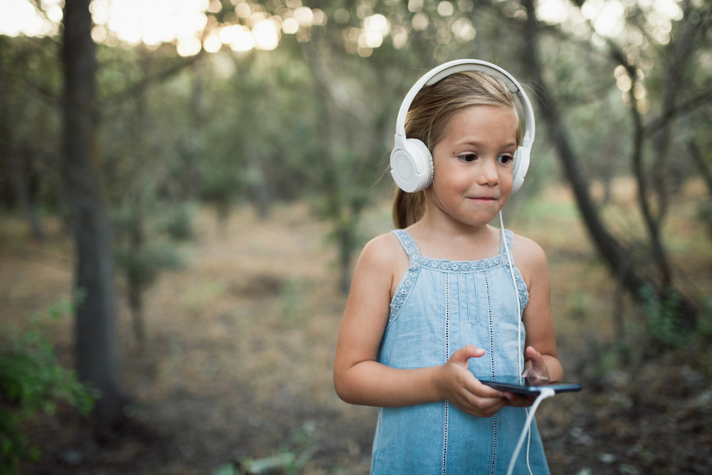 Little girl listening music with her smartphone and headphones in the forest