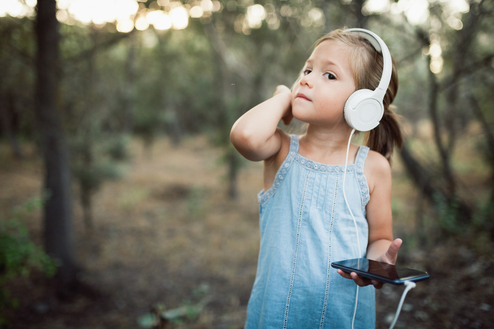 Little girl listening music with her smartphone and headphones in the forest