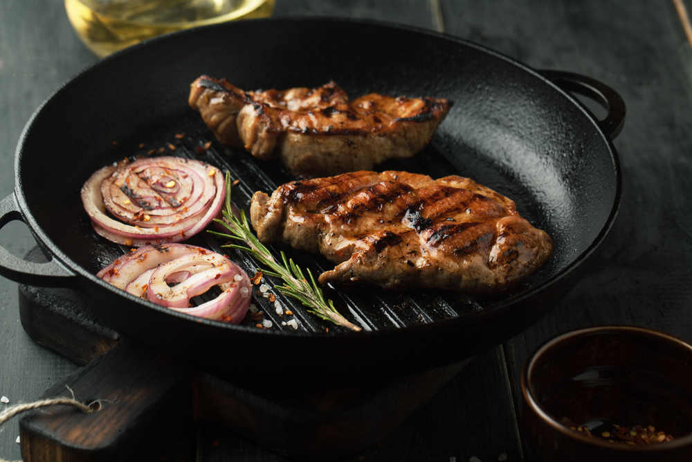Grilled steak of pork with spices, rosemary and chili pepper in a frying pan on a dark background
