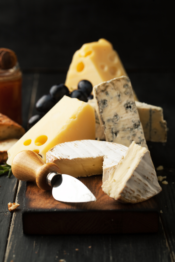 Assorted cheeses with grapes, nuts and rosemary on a wooden background