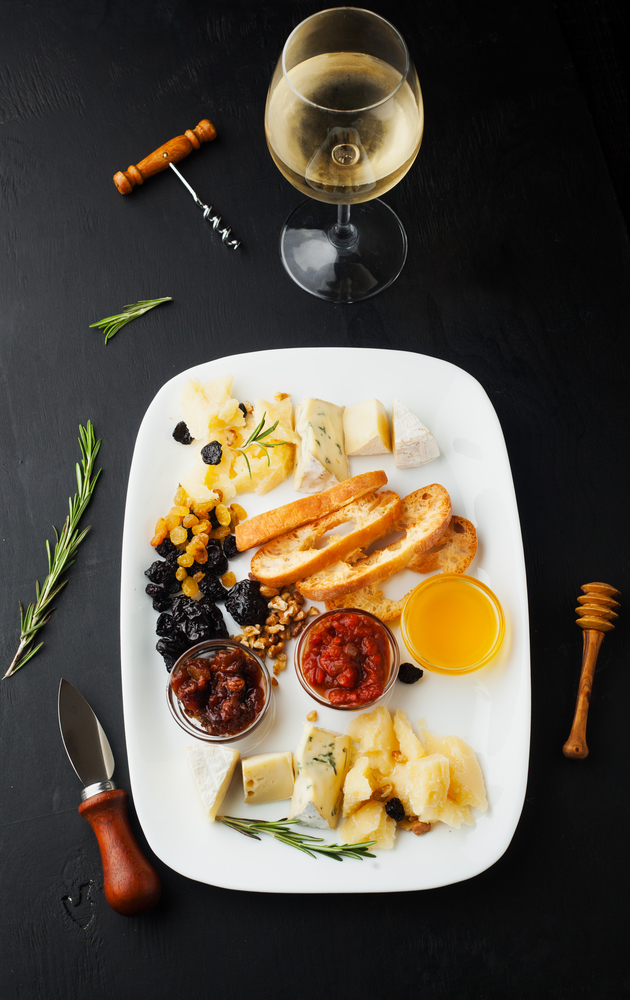 Cheese platter with honey, nuts and a glass of wine on a dark background