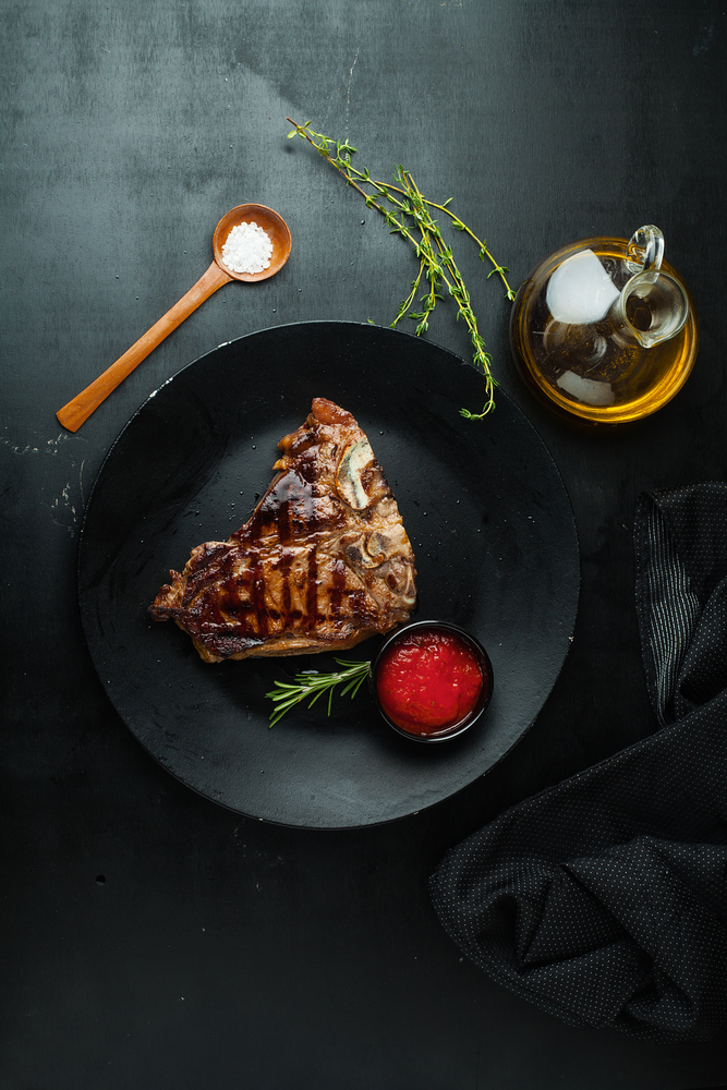 Grilled steak t-Bone on a plate with sauce, olive oil and rosemary on a dark background