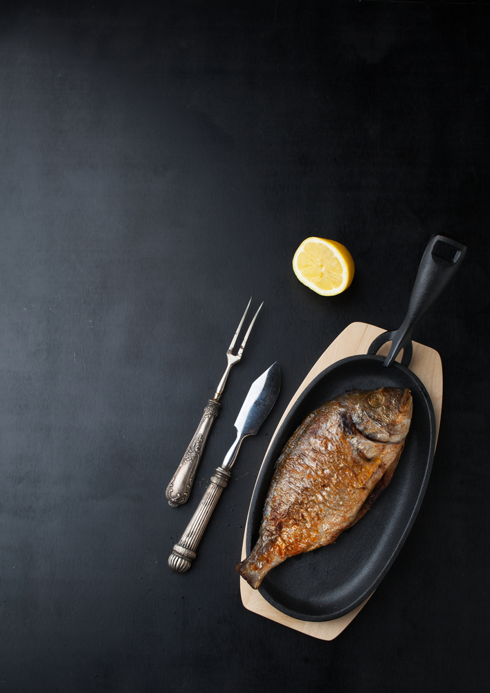 Baked fish dorado with lemon on a dark background