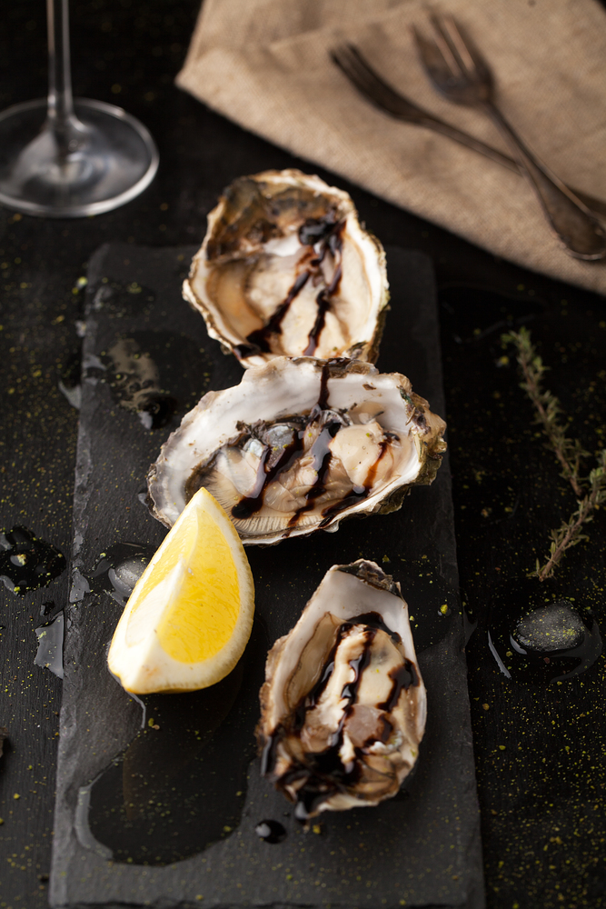 Fresh oysters with lemon and glasses of wine on a dark background
