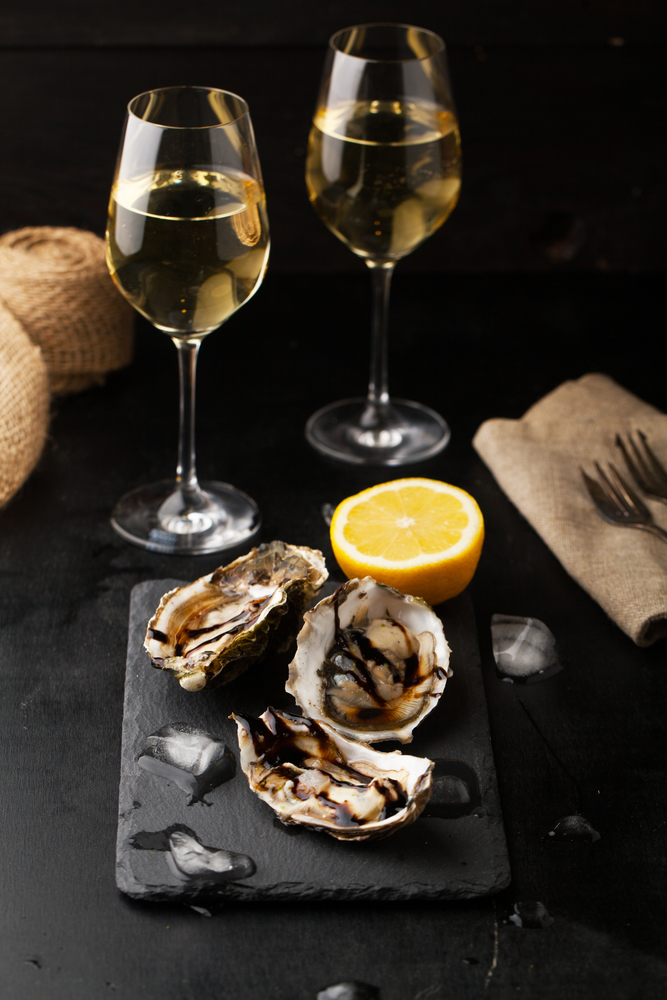 Fresh oysters with lemon and a glass of wine on a dark background