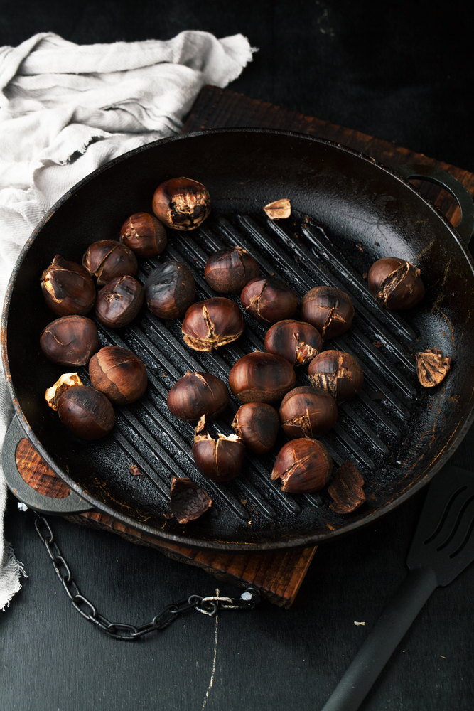 Grilled chestnuts in a frying pan on a dark background