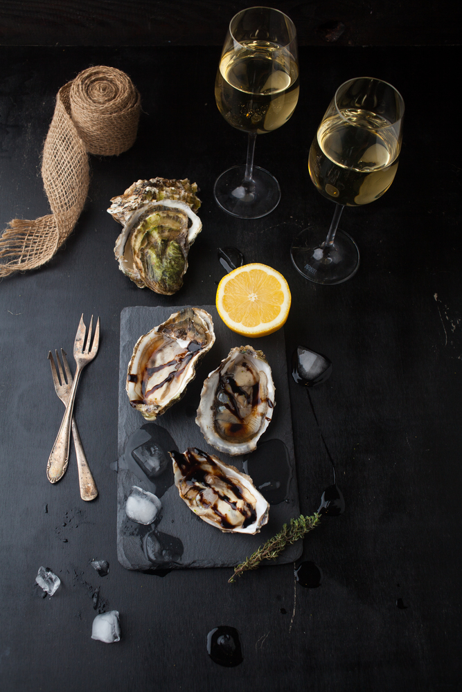Fresh oysters with lemon and a glass of wine on a dark background