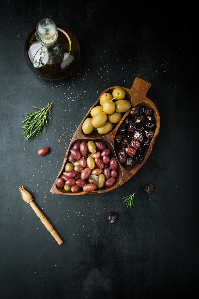 Bottle of olive oil, assorted of marinated olives with herbs and rosemary on a dark background
