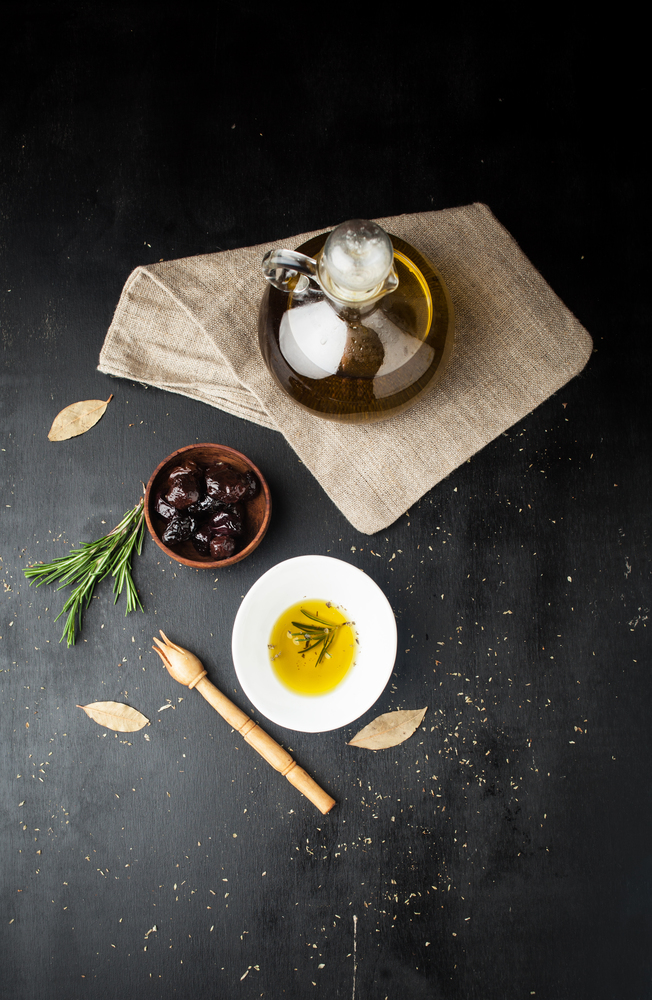Bottle of olive oil, marinated olives with herbs and rosemary on a dark background