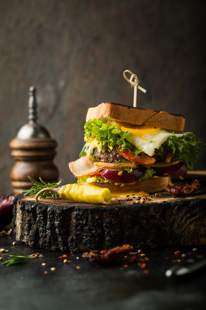 Delicious sandwich with bacon, tomatoes, egg and salad on a dark background
