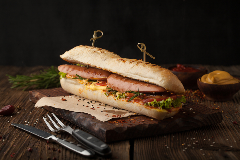 Delicious grilled hot dog with sausage and bacon, ketchup and mustard on a wooden background