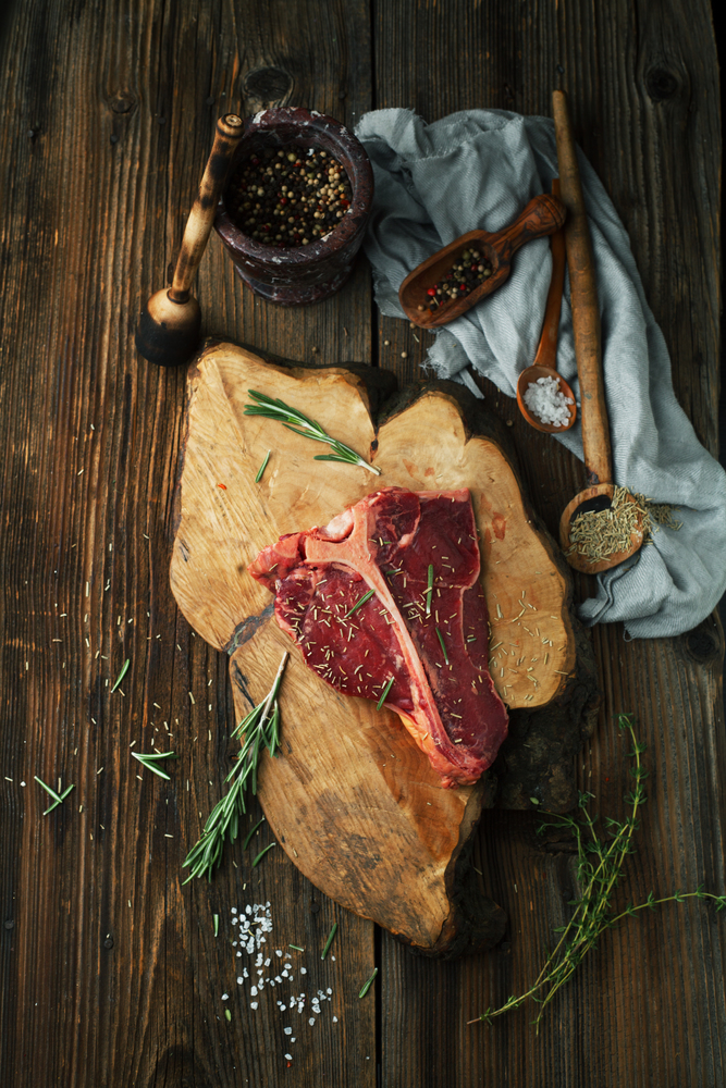 Raw Steak T-Bone with oregano and rosemary, salt, pepper and ketchup on the wooden table