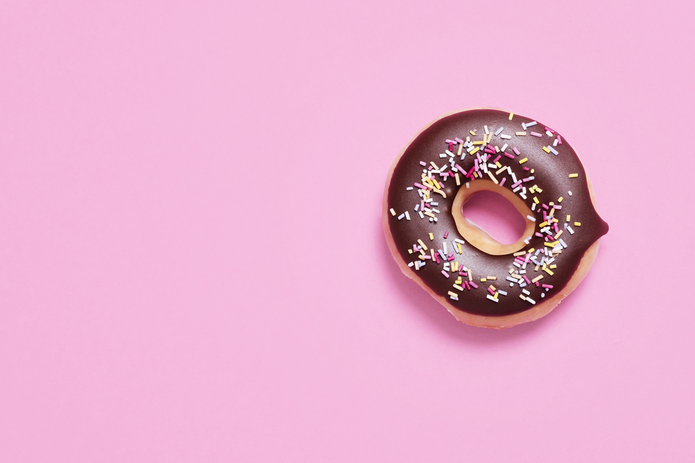 Single donut, doughnut with chocolate glaze and sprinkles offset on a pink background shot from above with copy space and room for text