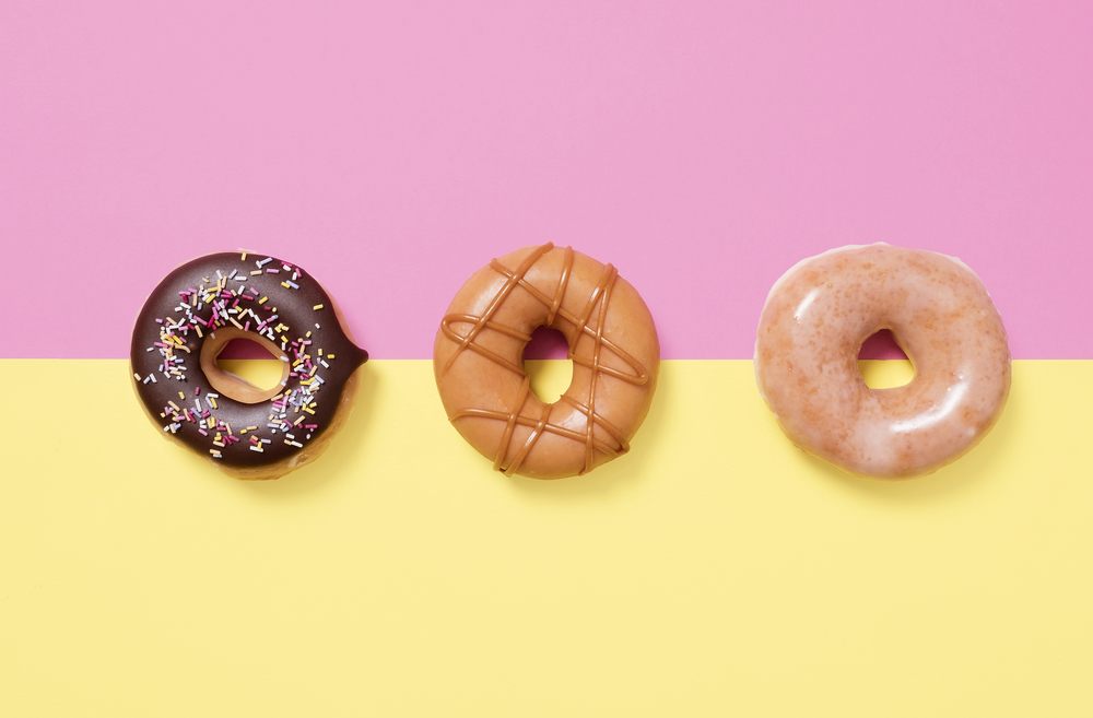 Three donuts, doughnuts, on a split coloured pink and yellow background shot from above with copy space and room for text