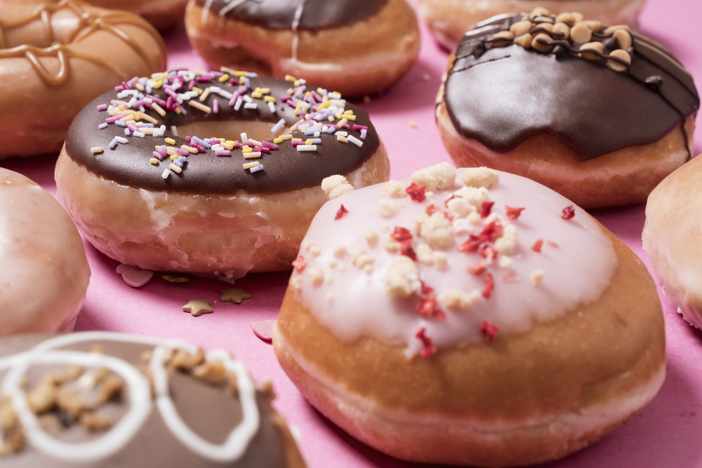 Assorted donuts, doughnuts, on a pink background with sprinkles and chocolate and glaze