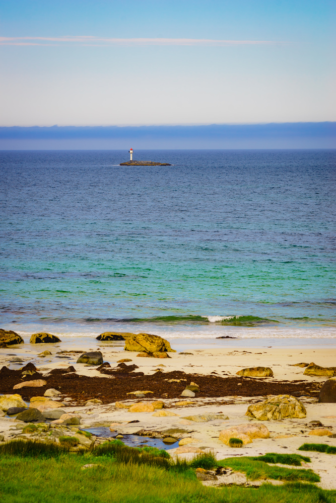 Seascape sandy beach sea shore with lighthouse on horizon. Andoya island Bleiksstranda beach. Vesteralen archipelago, Norway.. Seascape sandy beach with lighthouse on horizon