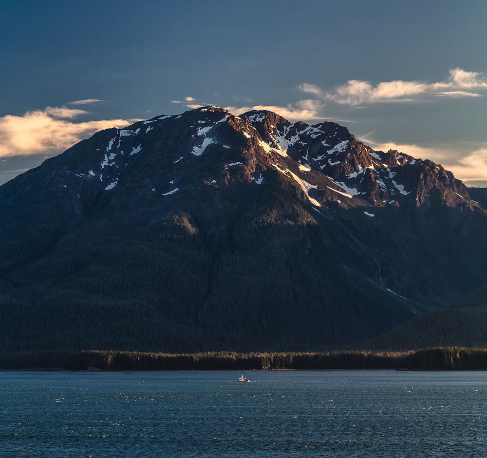 Massive mountain at sunset with a small boat sailing by it in Alaska