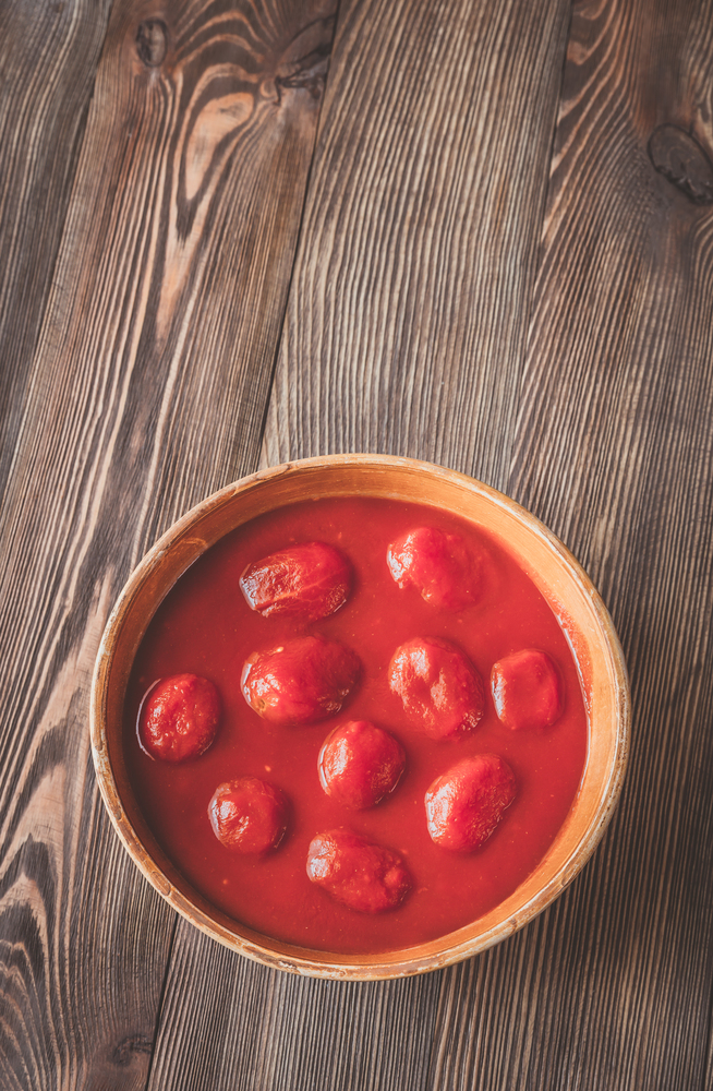 Bowl of canned tomatoes on the wooden background
