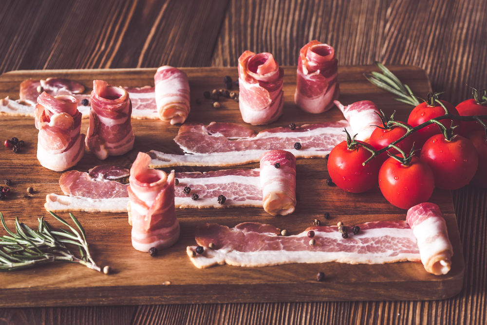 Bacon strips with cherry tomatoes and rosemary on the wooden board