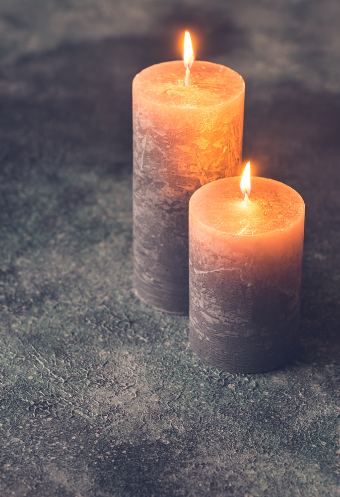 Two burning candles on gray background