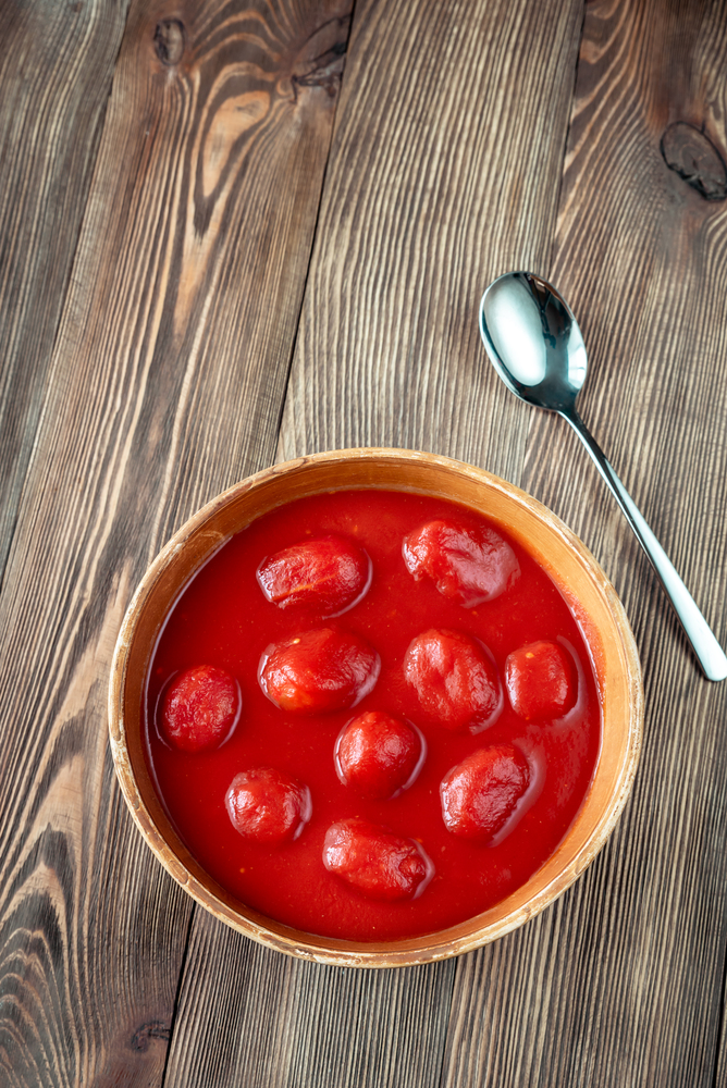 Bowl of canned tomatoes on the wooden background