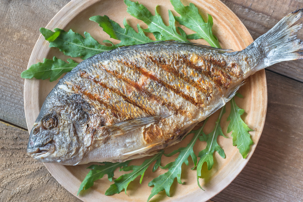 Grilled gilt-head bream with fresh arugula on the plate