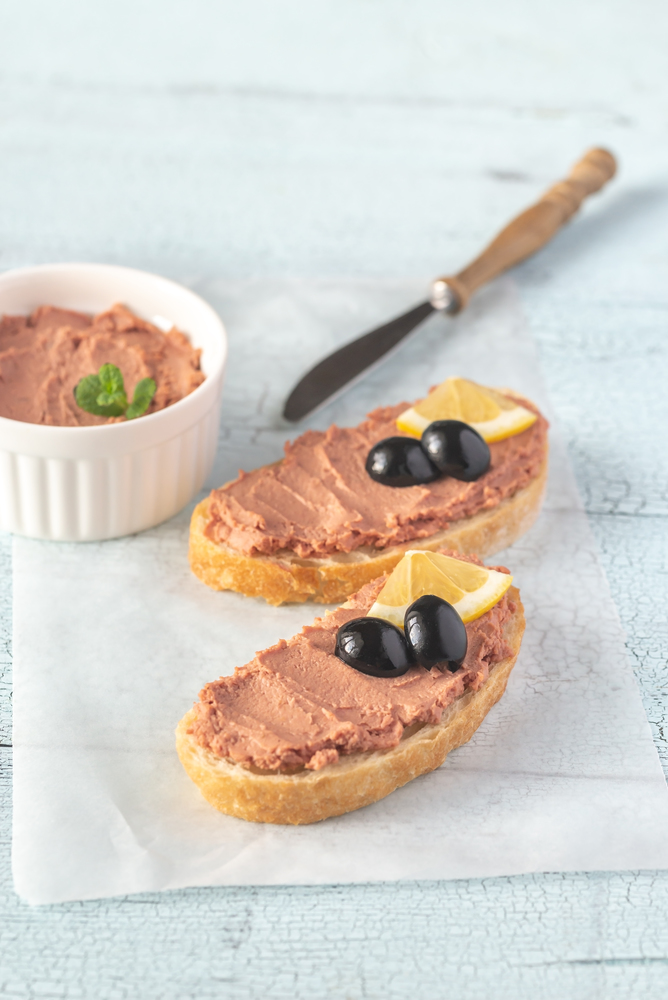 Sandwich with chicken liver pate and black olives on the white parchment