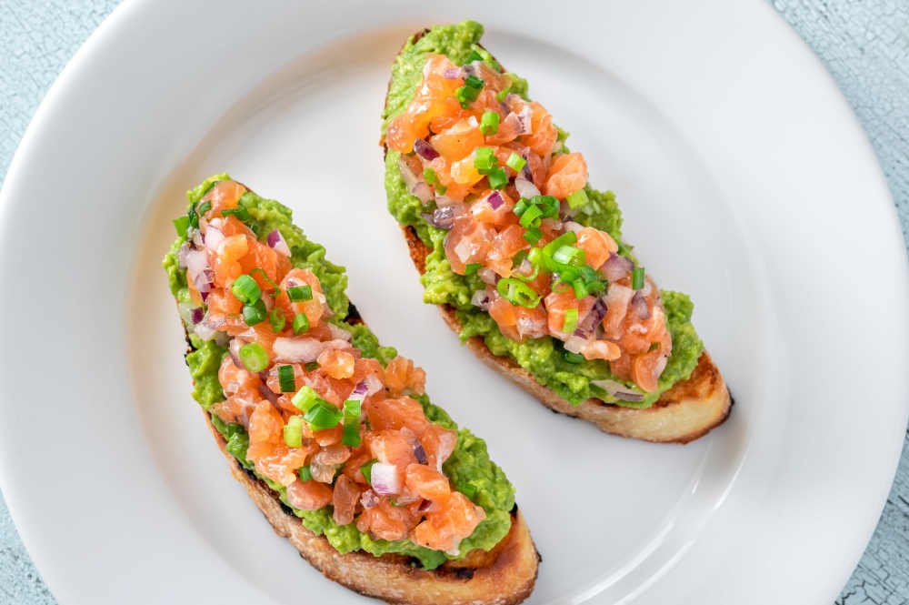 Two guacamole and salmon toasts on white plate
