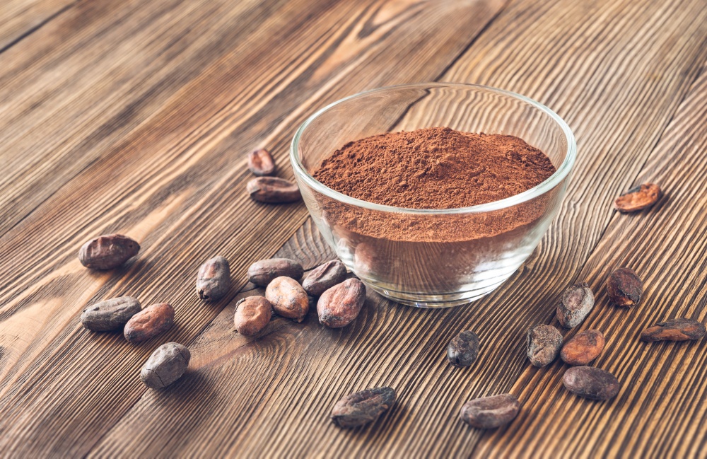 Glass bowl of cocoa powder with cocoa beans