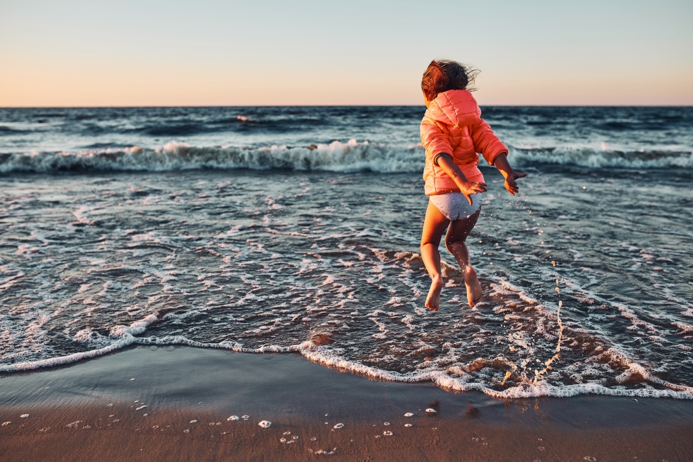 Playful little girl jumping over sea waves on a sand beach at sunset during summer vacation. Playful little girl jumping over sea waves on a sand beach at sunset