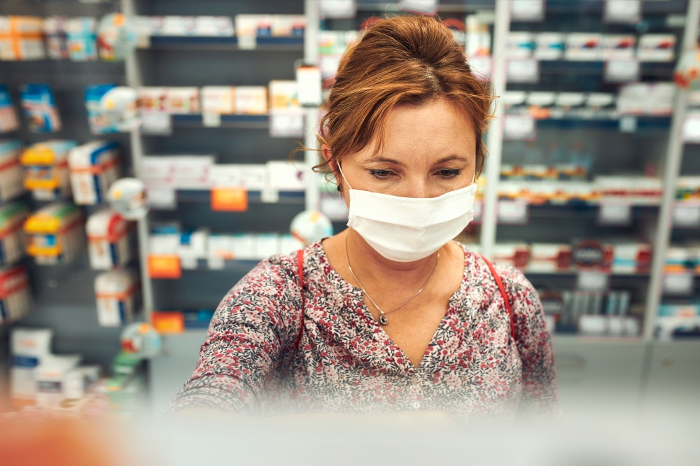 Woman shopping at pharmacy, buying medicines, wearing face mask to cover mouth and nose during pandemic coronavirus outbreak
